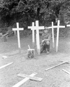 12 juillet 1944 : un prisonnier allemand peint des croix en bois au cimetière militaire d'Orglandes. Photo : US National Archives