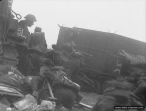 Des soldats britanniques à l'abri derrière un Universal Carrier sur le secteur de plage Queen de Sword Beach. Photo: IWM