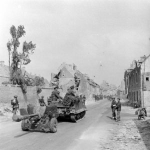Juillet 1944 : dans les ruines de la ville de Caen, un véhicule Universal Carrier canadien, précédé par des motocyclistes, remorque un canon antichar Ordnance QF 6-Pounder. De part et d'autres, des militaires canadiens progressent en colonne. Photo : George Rodger pour LIFE Magazine