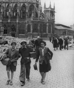 Le long de l'actuel boulevard des Alliés à Caen, des civils et des membres de la Défense passive (casque blanc) apportent leur aide à des réfugiés. L'église Saint-Pierre est visible en arrière-plan. Photo : DR