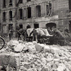 Juillet 1944 : rue de Bayeux à Caen, des civils et des militaires aident un transport de vivres à traverser les décombres. Photo : DR