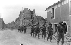 Juillet 1944 à Caen : sous la chaleur estivale, une colonne de soldats canadiens progresse le long de la rue du général Moulin. Photo : George Rodger pour LIFE Magazine