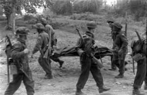 Juillet 1944 : des soldats canadiens dans Caen évacuent un de leurs blessés sur un brancard. Ils sont situés dans le secteur de l'actuelle rue de l'Arquette. Photo : George Rodger pour LIFE Magazine