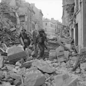 Le 9 juillet 1944 à Caen, des soldats canadiens, dont au moins un brancardier, se frayent un chemin dans les ruines. Photo : IWM B 6727