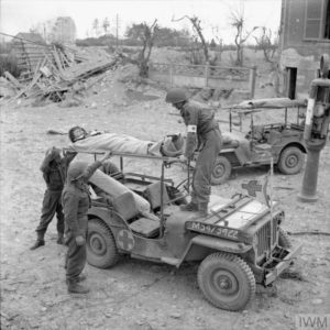 10 juillet 1944 : un blessé anglais de la 3rd (GB) Infantry Division est chargé à bord d'une Jeep médicalisée dans le secteur de Caen. Photo : IWM B 6826