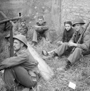 19 juillet 1944 : dans la périphérie de Caen, des soldats canadiens surveillent des prisonniers allemands qui sont accompagnés par une civile française. L'un des Allemands porte un pantalon camouflé et pourrait appartenir à la Waffen SS. Photo : IWM B 7748