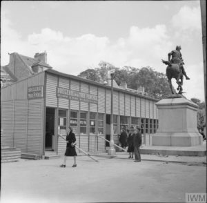 En 1945 à Caen, place Saint-Martin, le magasin "La Brûlerie de la Tour Penchée" a pris place dans des locaux préfabriqués en bois, à proximité de la statue Duguesclin. Le commerce a peu à peu repris au milieu des ruines grâce à ces installations sommaires. Photo : IWM BU 7885