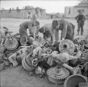 Juillet 1944 : sur les quais des chantiers navals de Caen, des prisonniers allemands récupèrent les pièces pouvant l'être parmi plusieurs essieux de camions. Photo : IWM BU 7882