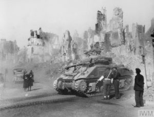 Juillet 1944 : un char M4 Sherman canadien traverse les ruines de la ville de Caen en soulevant un nuage de poussière. Photo : NYT 12797E