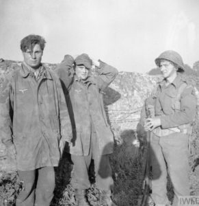 11 juillet 1944 : un soldat canadien de la 3rd (CA) Infantry Division prend la pose avec deux prisonniers allemands dans la banlieue de Caen. Photo : IWM B 6861