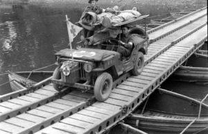 Le 19 juillet 1944 à Caen, à hauteur de l'actuelle rue de l'Arquette, une Jeep médicalisée transporte trois blessés canadiens en traversant l'Orne sur un pont de bateaux. Le véhicule appartient à la No. 14 Field Ambulance, Royal Canadian Army Medical Corps (RCAMC), 3rd (CA) Infantry Division. Photo : George Rodger pour LIFE Magazine