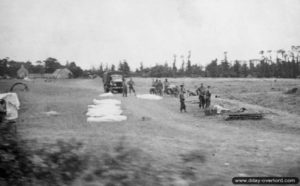 28 juin 1944 : le cimetière temporaire de Carquebut, à proximité de Donville. La population civile locale aide les Américains à procéder aux inhumations. Au départ, les corps sont enterrés dans de simples parachutes puis dans des sacs mortuaires. L’éloignement de la ligne de front permet l’inhumation dans des cercueils. Les premiers corps ont ainsi été déterrés afin d’être placés dans des cercueils en bois. Photo : US National Archives