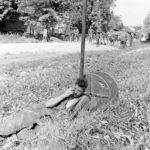 18 juillet 1944 : à l'extrémité sud de la commune de Bénouville, entre le pont "Pegasus" et le pont "London Bridge 1" sur le canal de Caen à la mer, un sapeur britannique prend quelques minutes de répit sous la chaleur estivale. En arrière-plan, d'autres sapeurs transportent des éléments de pont Bailey. Photo : George Rodger pour LIFE Magazine