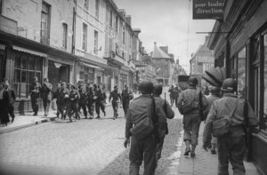 Des militaires américains, casqués et armés, croisent des militaires britanniques, sans casque ni arme, à Bayeux rue Saint-Jean, après la libération durant l'été 1944. Photo : LIFE Magazine