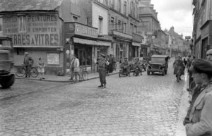 La police militaire britannique règle la circulation à l'angle de la rue Royale et de la rue Alain Chartier à Bayeux durant l'été 1944. Photo : LIFE Magazine