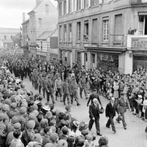 Défilé rue du maréchal Foch à Bayeux le 14 juillet 1944. En tête du cortège de gauche à droite : Monsieur Riby, président intérimaire de la Cour d'appel de Caen, François Coulet, Commissaire de la République, et Pierre de Chevigné, commandant le groupe de subdivisions libérées. Second rang : Raymond Triboulet, sous-préfet de Bayeux. Troisième rang : militaires britanniques, américains et français. Quatrième rang : anciens combattants français. Photo : George Rodger pour LIFE Magazine