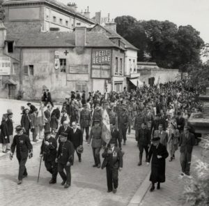 Défilé rue du maréchal Foch à Bayeux le 14 juillet 1944. Derrière le premier rang d'anciens combattants : monsieur Riby, président intérimaire de la Cour d'appel de Caen, François Coulet, Commissaire de la République, et Pierre de Chevigné, commandant le groupe de subdivisions libérées. Derrière eux, le rang des militaires britanniques, américains et français. Photo : DR