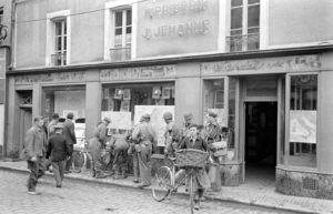 Des militaires américains et britanniques ainsi que des civils devant l'imprimerie J. Jehanne, rue Saint-Malo à Bayeux durant l'été 1944. Photo : LIFE Magazine