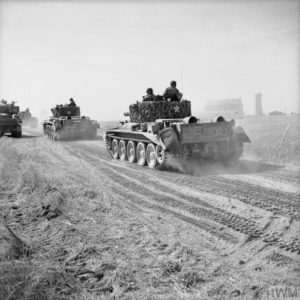 Des chars Cromwell appartenant au 2nd Northamptonshire Yeomanry de la appartenant à la 11th (GB) Armoured Division contournent Ranville par l'est en direction d'Escoville le 18 juillet 1944 pendant l'opération Goodwood. Les ruines de l'église de l'Assomption Notre-Dame sont visibles en arrière-plan. Photo : IWM B 7563