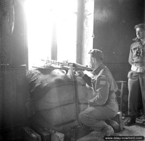 20 juin 1944 : le caporal W. Lennox du Queen’s Own Rifles of Canada épaule une mitrailleuse MG 42 dans une maison de Bretteville-l’Orgueilleuse. Photo : IWM