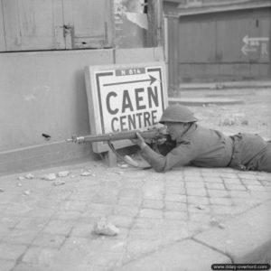 Un soldat se plaque au sol à la recherche d’un tireur isolé adverse dans Caen. Photo : IWM