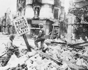 Un lieutenant et un autre soldat du Royal Ulster Rifles observent un panneau de signalisation au milieu des ruines. Photo : IWM