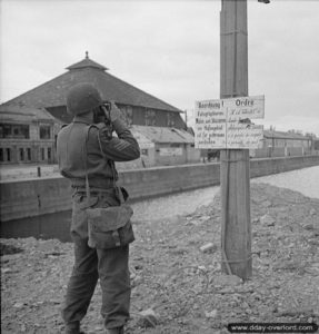 Le sergent Jimmy Mapham de la No 5 Army Film and Photographic Unit prend un photo un panneau allemand interdisant toute prise de photo dans le port de Caen. Photo : IWM