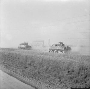 18 juillet 1944 : des chars Sherman du 23rd Hussars, 11th Armoured Division, traversent le découvert devant l’usine métallurgique pendant l’opération Atlantic. Photo : IWM