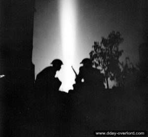25 juillet 1944 : pendant le tir de barrage de l’artillerie britannique lors de l’opération Spring, des soldats progressent en direction de la ligne de débouché. Photo : IWM