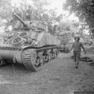 18 juillet 1944 : des chars Sherman du Staffordshire Yeomanry, 27th Armoured Brigade, transportant des soldats de la 3rd Division, se déplacent pour rejoindre le point de départ de l’opération Goodwood, dans le secteur de Hérouvillette. Photo : IWM