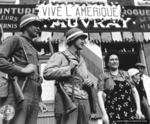 Rue de Balleroy, deux policiers militaires américains devant la droguerie tenue par A. Auvray au Molay-Littry. Photo : US National Archives