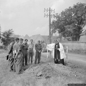 Un aumônier anglais et des soldats rendent un dernier hommage à un camarade pendant que des chars du 8th Hussars progressent en direction de Lisieux. Photo : IWM