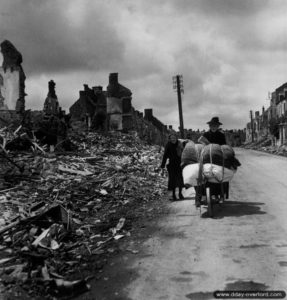 15 juin 1944 : des civils normands chargés par leurs biens transportables les plus précieux marchent le long d’une rue dégagée de la commune dévastée de Pont-l’Abbé. Photo : US National Archives