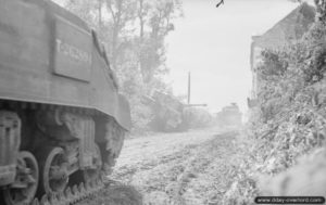 28 juin 1944 : des chars Sherman du 1st Nottinghamshire Yeomanry (Sherwood Rangers), 8th Armoured Brigade, dépassent l’épave du char Tigre « 334 » à Rauray détruit pendant l’opération Epsom. Photo : IWM