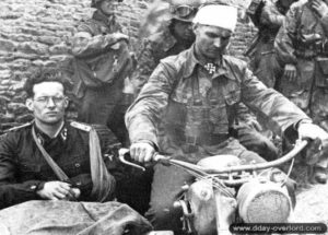 9 juin 1944 : à Rots, le SS-Hauptsturmführer Rudolf von Ribbentrop, 3. Kompanie, I./SS-PzRgt 12 dans un sidecar piloté par le SS-Obersturmbannführer Max Wünsche, commandant le SS-PzRgt 12, après une visite à la troisième section de la 15/25, sévèrement touchée par les combats. Photo : Bundesarchiv