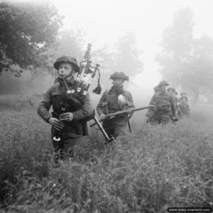 26 juin 1944 : des soldats du 7th Seaforth Highlanders, 15th (Scottish) Division, guidés par un piper sonnant de la cornemuse au début de l’opération Epsom dans le secteur de Saint-Manvieu-Norrey. Photo : IWM