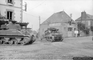 31 juillet 1944 : un char Sherman laisse passer un Loyd Carrier remorquant un canon anti-char QF 6-Pounder à Saint-Martin-des-Besaces. Photo : IWM