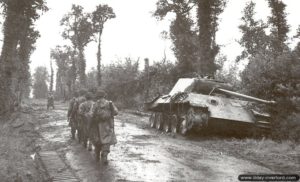 Des soldats anglais progressent vers le front à proximité d’un char Panther A détruit le 15 juin 1944 dans le secteur de Tilly-sur-Seulles. Photo : IWM
