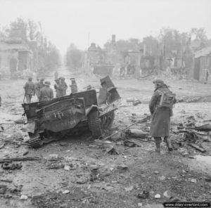 19 juin 1944 : un sapeur anglais inspecte les abords d’un Universal Carrier détruit par une mine dans la localité de Tilly-sur-Seulles. Photo : IWM