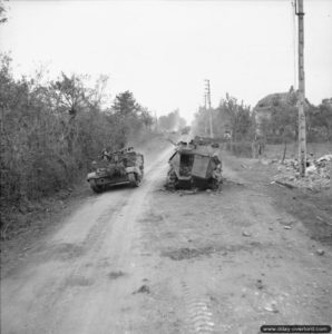 19 juillet 1944 : un Universal Bren Carrier progresse à proximité d’un véhicule SdKfz 250 détruit près de Troarn pendant l’opération Goodwood. Photo : IWM