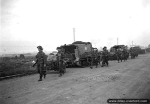 25 juillet 1944 : des soldats canadiens croisent des Carriers remorquant des canons antichar au sud de Vaucelles. Photo : Archives Canada
