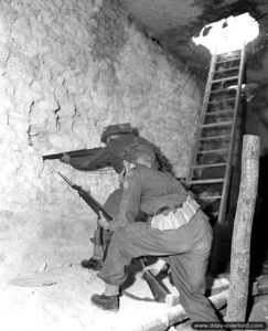 23 juillet 1944 : les soldats D. H. Holmes et W. J. Wilkinson surveillent les environs à l’abri d’un bâtiment de Vaucelles. Photo : Archives Canada