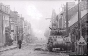 L’épave du char Sherman PC du Major Well dans la rue principale de Villers-Bocage. Le canon factice en bois, permettant de dissimulé le Sherman commandement au sein des escadrons, est tombé à terre. Photo : Bundesarchiv