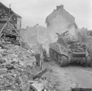 Un char Sherman progresse dans les ruines de Putanges devant les habitants normands. Photo : IWM