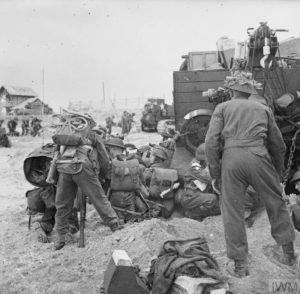 Des transmetteurs britanniques à l'abri derrière un Universal Carrier sur le secteur de plage Queen de Sword Beach. Photo: IWM B5094