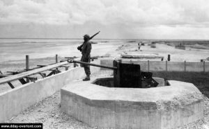Une sentinelle à Utah Beach en 1945 devant un encuvement pour canon antichar de 50 mm. Photo : US National Archives