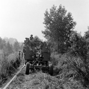 Dans le secteur de Blainville-sur-Orne le 18 juillet 1944 (jour du déclenchement de l'opération Goodwood), un canon antiaérien Bofors de 40 mm baptisé "Paname" et appartenant à la Troop G de la 113th Light Anti-Aircraft Battery (370th Light Anti-Aircraft Regiment) est tracté par un camion britannique le long d'une piste balisée. La pièce va se mettre en position pour défendre les deux points de franchissement "Tay 1" et "Tay 2" sur l'Orne et le canal de Caen à la mer. Photo : Ralph Morse pour LIFE Magazine