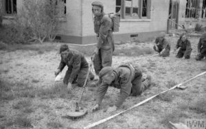 15 juillet 1944 : des sapeurs anglais déminent les abords d'un ancien hôtel de luxe qui est utilisé pour l'hébergement des militaires de la 3rd (GB) Infantry Division. Photo : IWM B 7342