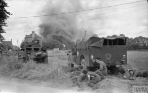 July 26, 1944: a shell hit an ammunition depot in Normandy. British soldiers find refuge behind an M3 Scout Car (right) and a Staghound reconnaissance vehicle, fearing new explosions. Photo: IWM B 8148