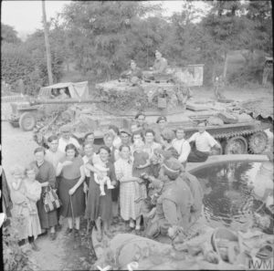 18 août 1944 : des équipages britanniques de chars Cromwell appartenant au 2nd Northamptonshire Yeomanry (11th Armoured Division) en compagnie de civils normands pendant la progression de leur unité, à côté d'une fontaine et d'un monument aux Morts. Photo : IWM B 9362